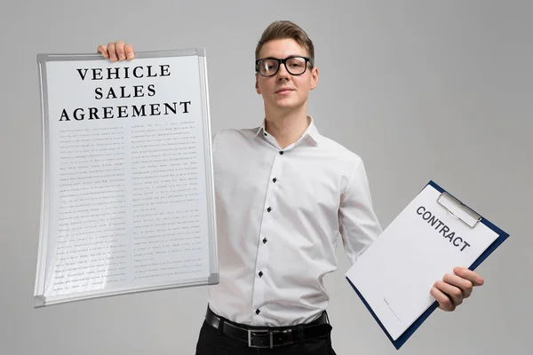 Junger Mann mit einem Fahrzeugkaufvertrag und leerem Vertragsformular isoliert auf hellem Hintergrund — Stockfoto
