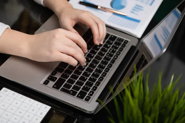 Close-up van vrouwelijke handen bezig met laptop grafieken met calculator op glanzend zwarte tabel analyseren — Stockfoto