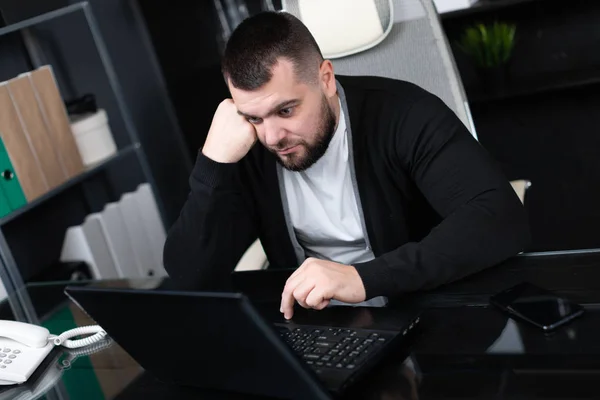 Портрет молодого человека, подпирающего голову кулаком с ноутбуком в бизнес-офисе — стоковое фото