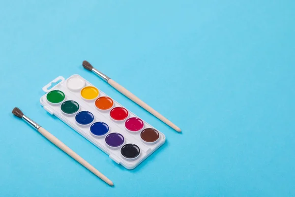 Pinturas y pinceles de acuarela en caja blanca, aislados sobre fondo azul —  Fotos de Stock