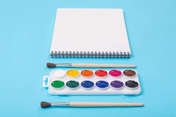 Conjunto de tintas aquarelle com pincéis e álbum para pintura isolada sobre fundo azul — Fotografia de Stock