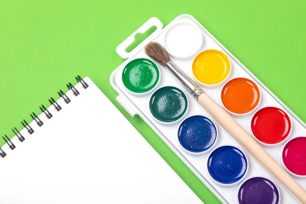 Aquarela tintas e pincéis com tela para pintura com copyspace sobre fundo verde — Fotografia de Stock