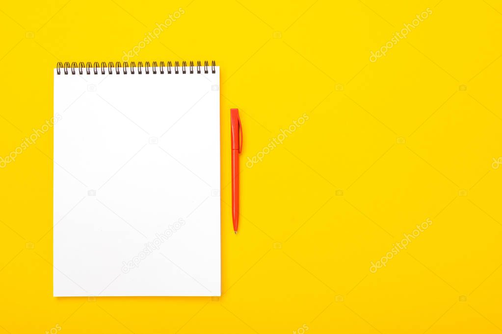 Working space table with notebook and pen with copyspace isolated on yellow background