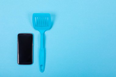 Mutfak parçası olarak çevrimiçi kavramı mavi zemin üzerine boşaltmak ile yemek, spatula ile üstünde hareket eden telefon