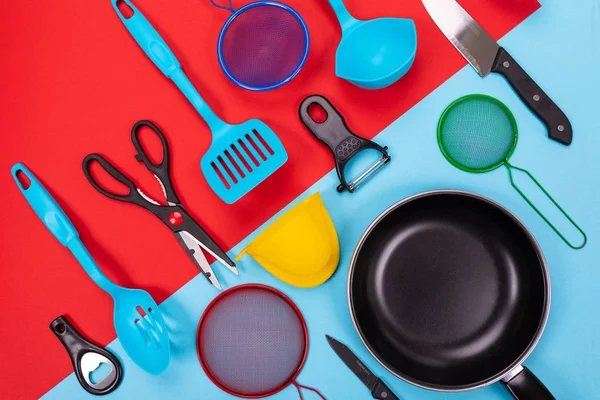 Close up portrait of frying pan with set of kitchen utensils on red-blue background — Stock Photo, Image