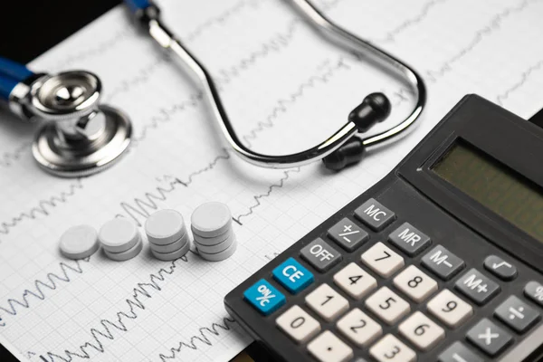 Estetoscópio, pílulas e calculadora estão em uma folha com um eletrocardiograma — Fotografia de Stock