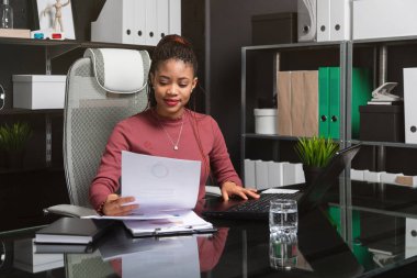 portrait of young black businesswoman working with charts and diagrams at Desk in office clipart