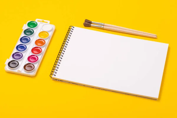 Акварельные краски и кисти с альбомом для рисования на желтом фоне — стоковое фото