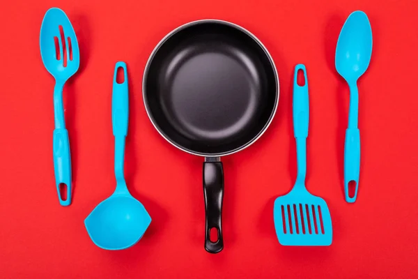 Koekenpan met keukengerei geïsoleerd op rode achtergrond — Stockfoto