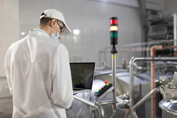 Человек в белом халате и маске с ноутбуком в руках на заводе — стоковое фото