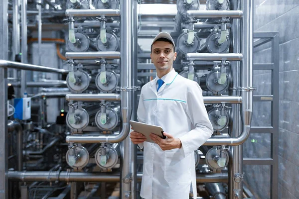 Man in a white robe with a tablet in his hands is in the production shop at the factory — Stock Photo, Image