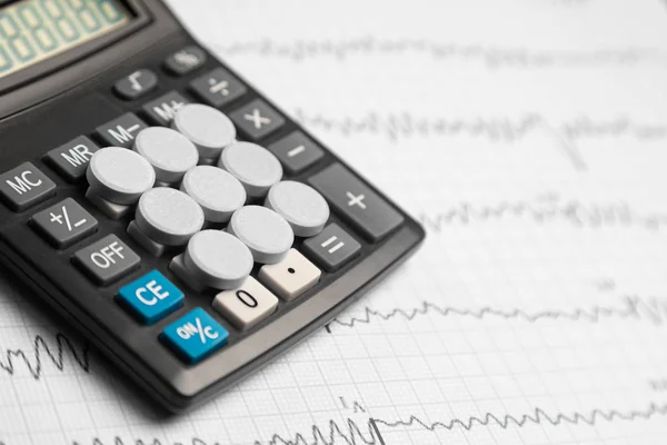 Tablets are on the calculator on background of electrocardiogram