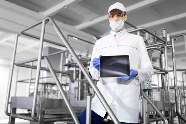 Человек в белом халате и маске с табличкой в руках на заводе — стоковое фото