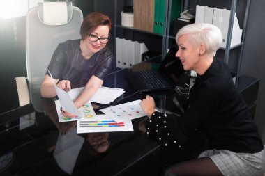 Business women discuss diagrams at Desk in office clipart