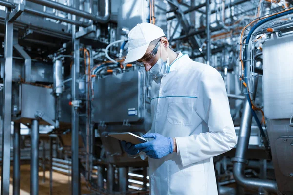 Человек в маске и халате стоит с табличкой в руках на молочном заводе — стоковое фото