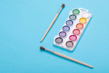 Suluboya resim yapıyor ve izole mavi zemin üzerine beyaz kutusunda, fırçalar