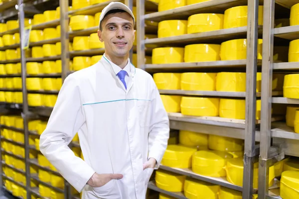 Hombre se encuentra en el fondo de bastidores de queso en la planta láctea —  Fotos de Stock