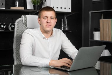 Genç adam ofiste dizüstü bilgisayarla çalışıyor.