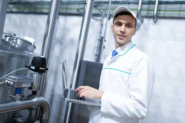 Mann im weißen Gewand mit Laptop in der Hand zwischen den Chromrohren — Stockfoto