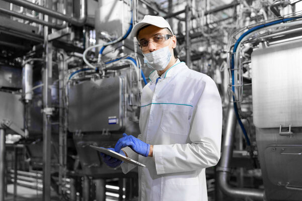 man in a mask and a Bathrobe stands with a tablet in his hands at the dairy Plant