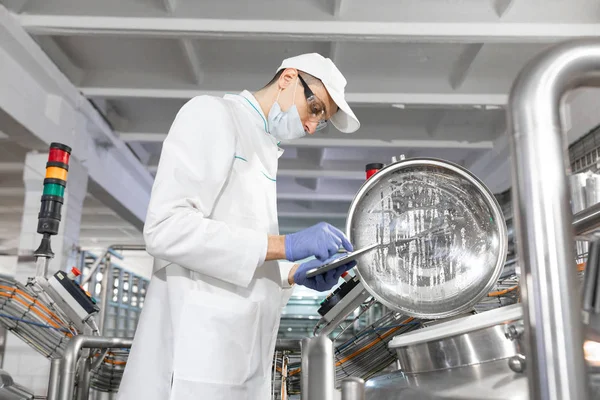 Man i en vit dräkt och en mask med en tablett i hans händer är nära kan i butiken — Stockfoto