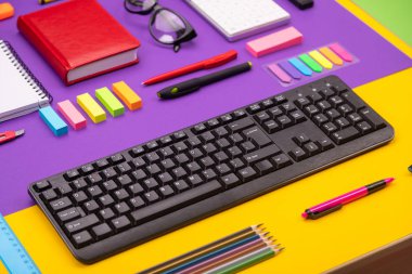 Klavye, günlüğü, kalem, kalem, turuncu-mor zemin üzerine gözlük ile modern çalışma yer. Üstten görünüm