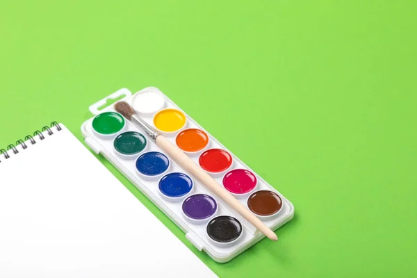 Акварельные краски и кисти с альбомом для рисования на зеленом фоне — стоковое фото