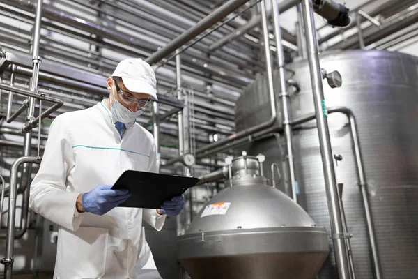 Technologue prenant les notes nécessaires tout en se tenant au département de production de l'usine laitière — Photo