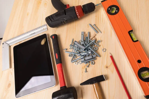 construction tool and a digital tablet lie on a light wooden table