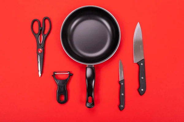 Koekenpan met keukengerei geïsoleerd op rode achtergrond — Stockfoto