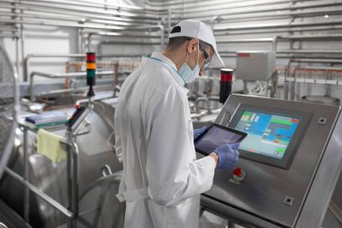 Technologist stands with a tablet near the digital screen at the dairy Plant clipart