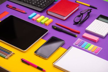 Tablet, hesap makinesi, Not defteri ve mor ve turuncu zemin üzerine smartphone ile modern çalışma yer. İş kavramı