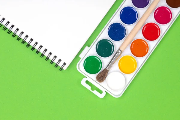 Акварельные краски и кисти с альбомом для рисования на зеленом фоне — стоковое фото