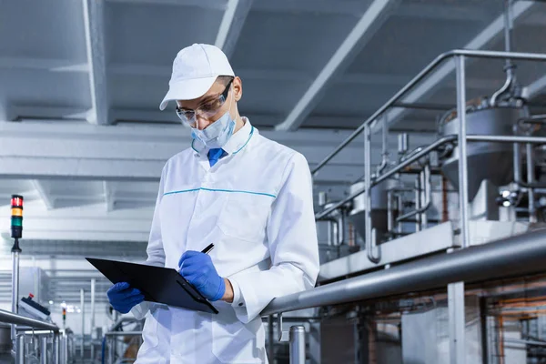 Uomo in una veste bianca e maschera prende appunti in piedi nel negozio — Foto Stock