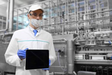 Yazmak için bir yer. Bir tablet ile fabrikada boş bir perde ile teknoloji uzmanı bir maske, eldiven ve beyaz bir elbise olarak duruyor. Dijital tablet üretim dükkanda üniformalı bir adam