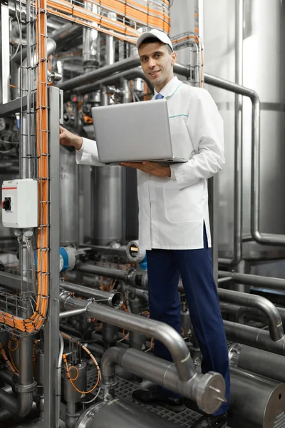 Homem em um manto branco com um laptop em suas mãos entre os tubos cromados — Fotografia de Stock