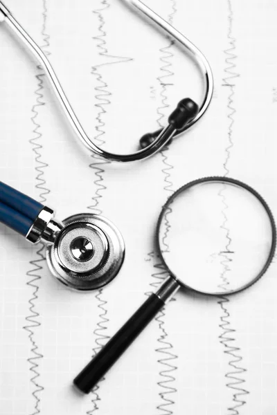 Stetoskop a zvětšovací sklo leží na list s EKG detailní pohled shora — Stock fotografie