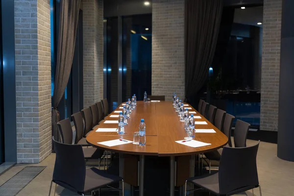 Oval wooden table with sheets of paper, water bottles and glasses next to them waiting for the conference