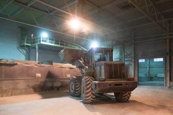 Трактор перемещает песок на цементном заводе. Темная комната с огнями — стоковое фото