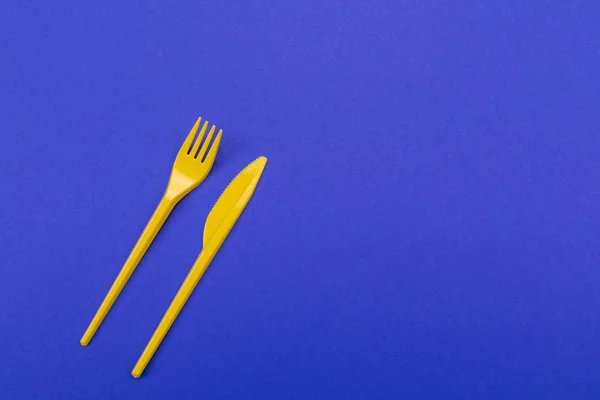 Conjunto de utensílios de mesa de garfo de plástico amarelo e faca isolado no fundo azul — Fotografia de Stock