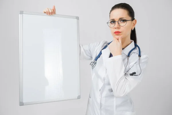 Brunette Frau im Arztkostüm mit einer Magnettafel in der Hand im Hintergrund — Stockfoto