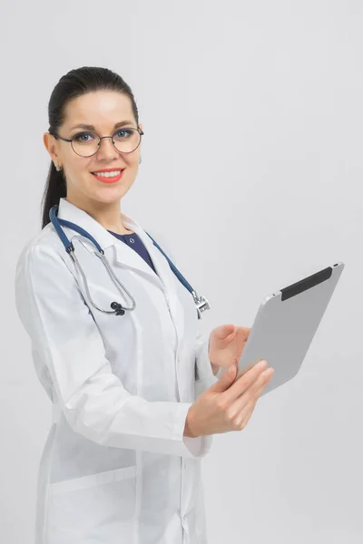 Ritratto di bruna in costume medico con una tavoletta moderna tra le mani isolata sullo sfondo — Foto Stock