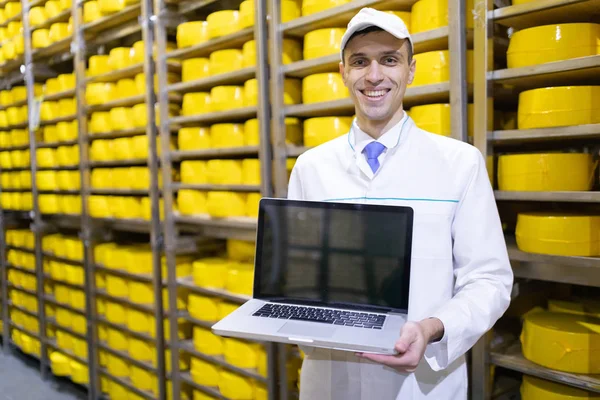 Portret van de mens in een wit gewaad en een GLB staande in productieafdeling van zuivelfabriek met laptop — Stockfoto