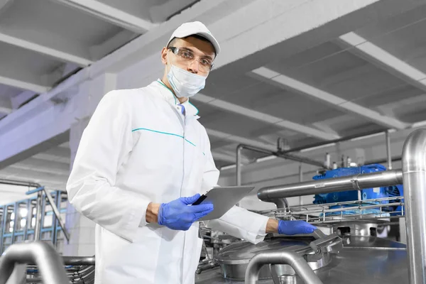 De man in een wit gewaad en een pet maken een inspectie van de productielijn — Stockfoto