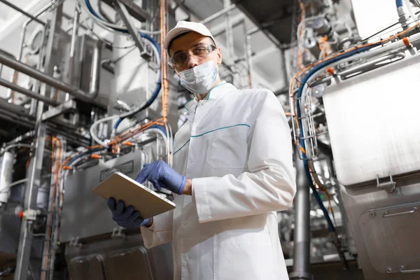 Hombre con una bata blanca y una gorra hacen una inspección de la línea de producción —  Fotos de Stock