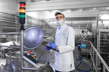 Bir maske ve bir scrub müfettiş elinde bir klasör-tablet ile süt fabrikasında duruyor