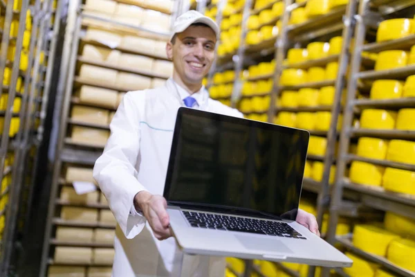 Retrato del hombre con una bata blanca y una gorra de pie en el departamento de producción de la fábrica de lácteos con ordenador portátil —  Fotos de Stock