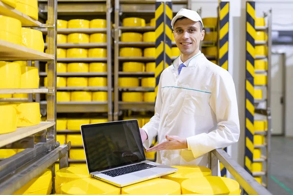 Portret van de mens in een wit gewaad en een GLB staande in productieafdeling van zuivelfabriek met laptop — Stockfoto