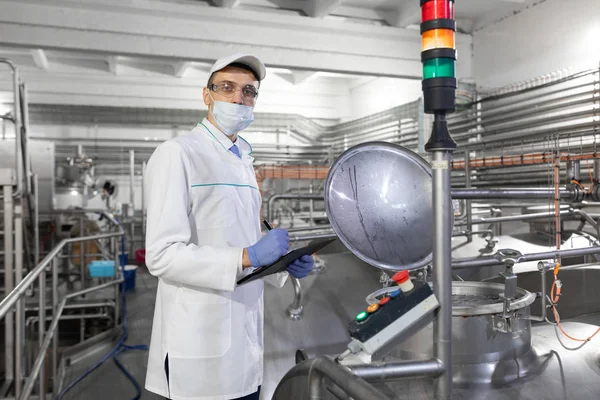 Inspektör i en mask och en skrubba står med en mapp-tablett i händerna på mejeri anläggningen — Stockfoto