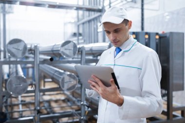 Gri tablet ile süt fabrikasının üretim bölümünde duran beyaz cüppe ve bir kap adam portresi